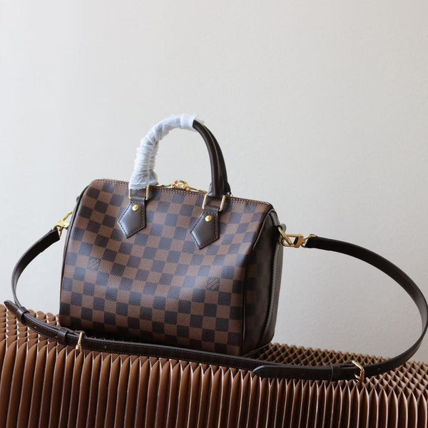 Pre-owned restored Louis Vuitton Damier Ebene Speedy 25 handbag with dark brown leather handles and strap, displayed on a sculpted tan surface.