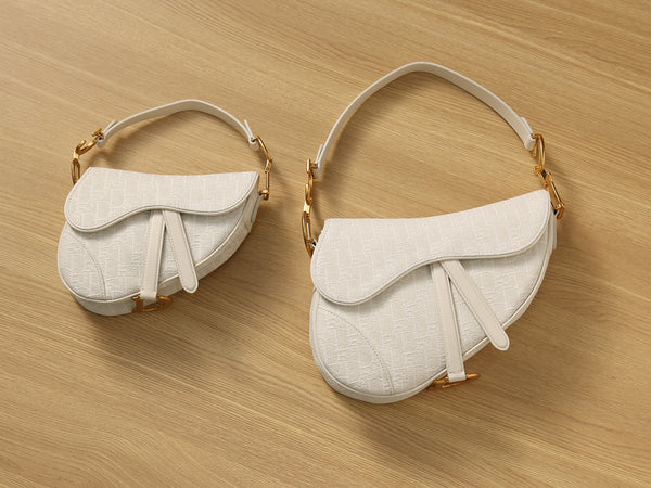 Two Empyrean restored used ivory Dior Saddle Bags in different sizes, placed side by side on wood background showcasing symmetry and texture.