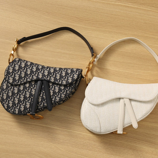 “Empyrean restored used Dior Saddle Bags in navy oblique and ivory canvas, displayed side by side on wood surface to showcase contrasting textures and restoration finish.”